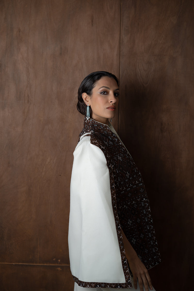 Nadya Shah BALTHAZAR CAPE jacket featuring a flowing design with intricate detailing, worn over a neutral outfit.