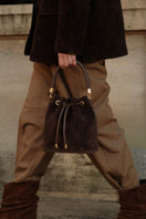 Saonara chocolate suede bucket shoulder bag with a rounded shape and adjustable strap, featuring stylish stitching and a spacious interior.