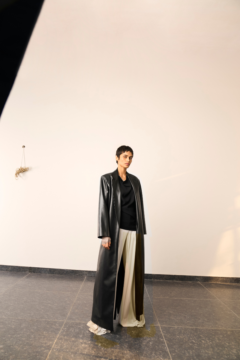 Black MADDIE trench coat by URA displayed on a hanger, showcasing its classic design and tailored fit.