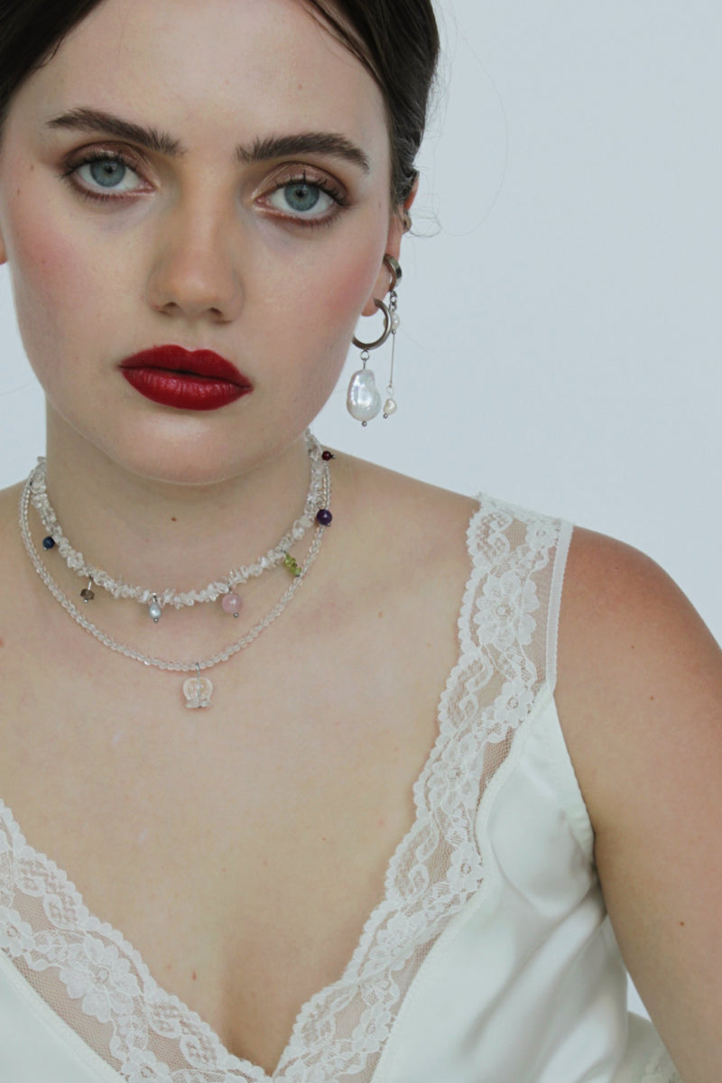 Aethera Alfonso Mix Charms Necklace in white featuring layered gold-tone chains with various charm pendants on a white background.