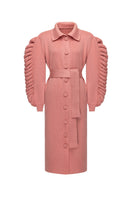 Liya dramatic pink knit belted coat hanging on a wooden background, featuring a textured knit fabric and a waist belt for style.