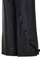 Black crossed leather pants by MAZ Manuela Álvarez, stylish slim-fit trousers with crossing design details, on a plain background.