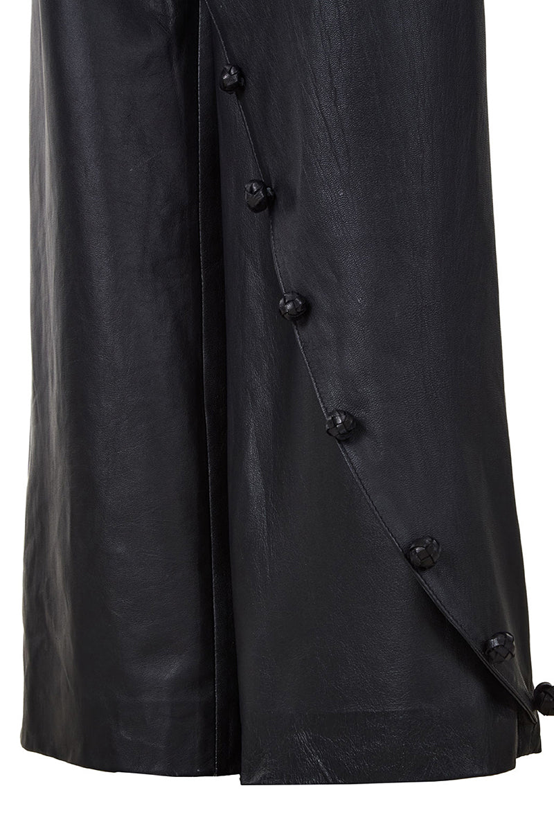 Black crossed leather pants by MAZ Manuela Álvarez, stylish slim-fit trousers with crossing design details, on a plain background.