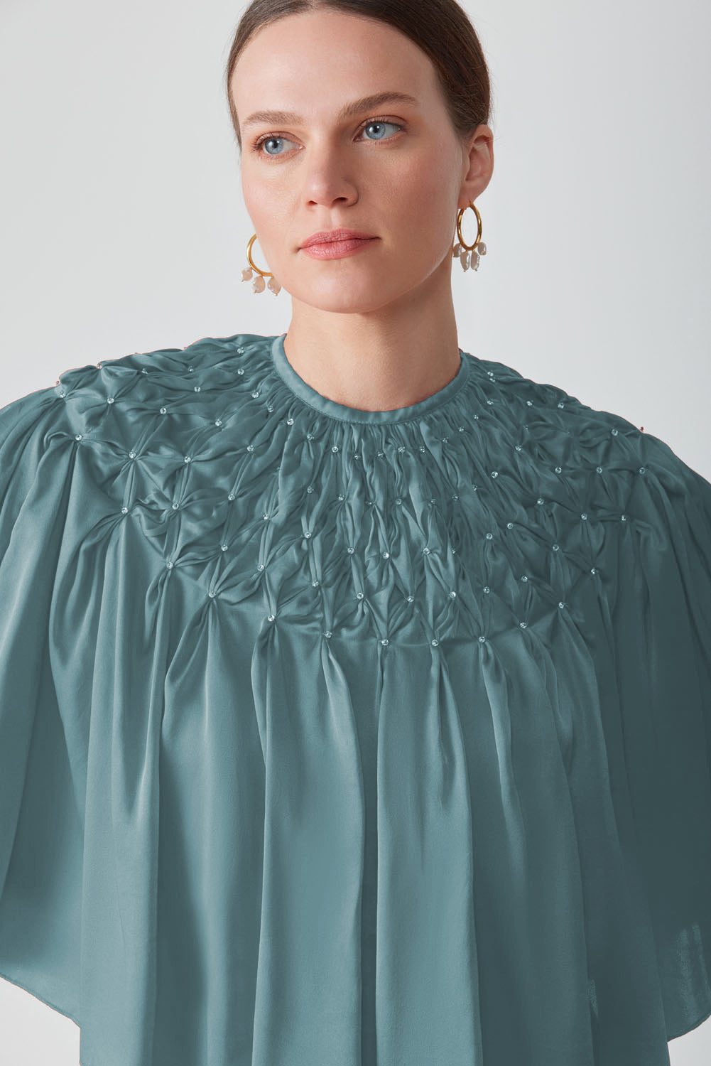 Hand-smocked cape in Saxon fabric by Mastani, featuring intricate detailing and a flowing design, perfect as a stylish top.