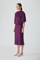 Hand-smocked aubergine cape top by Mastani with intricate stitching and flowing fabric, displayed on a neutral background.