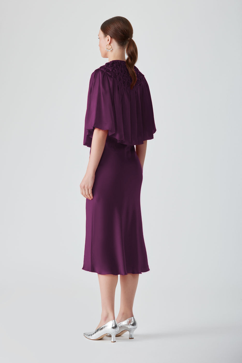 Hand-smocked aubergine cape top by Mastani, showcasing detailed craftsmanship and flowing fabric in a rich purple hue.