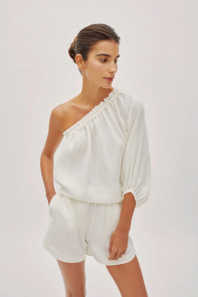 Labeca white linen shorts with a relaxed fit, styled with a one-sleeve top, perfect for casual summer wear.
