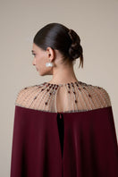 Long burgundy long sleeve gown by HACCHIC COUTURE displayed on a mannequin with elegant draping and a flowing silhouette.