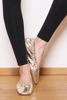 A pair of AERA Carla Gold Foil-Effect Flats showing their shiny, metallic gold finish and classic flat design on a white background.