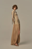 Poem Cascade gown in warm sand color, featuring flowing fabric and elegant design, worn by model in the image.