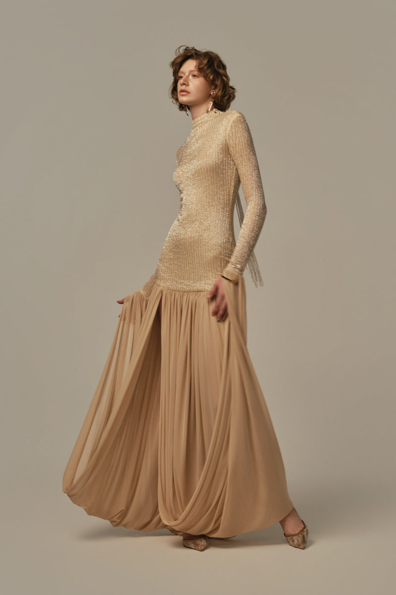 Poem Cascade Gown in Warm Sand color, elegant evening gown with flowing fabric and draped design, model wearing in a stylish setting.