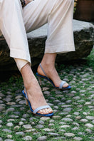 A pair of blue denim AERA Claudia slingback sandals with open toes and ankle straps on a neutral background.