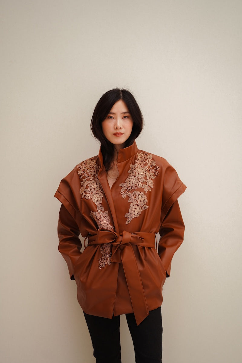 Nadya Shah Cleo faux leather belted jacket with a stylish collar and belt, shown on a hanger against a neutral background.