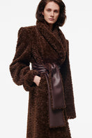Chocolate brown curly maxi coat by Kris Marán displayed on a model, showcasing its textured fabric and elegant length.