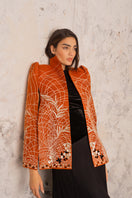 Nadya Shah Clementine Cape jacket in vibrant orange with wide collar and flowing design, displayed on a hanger.