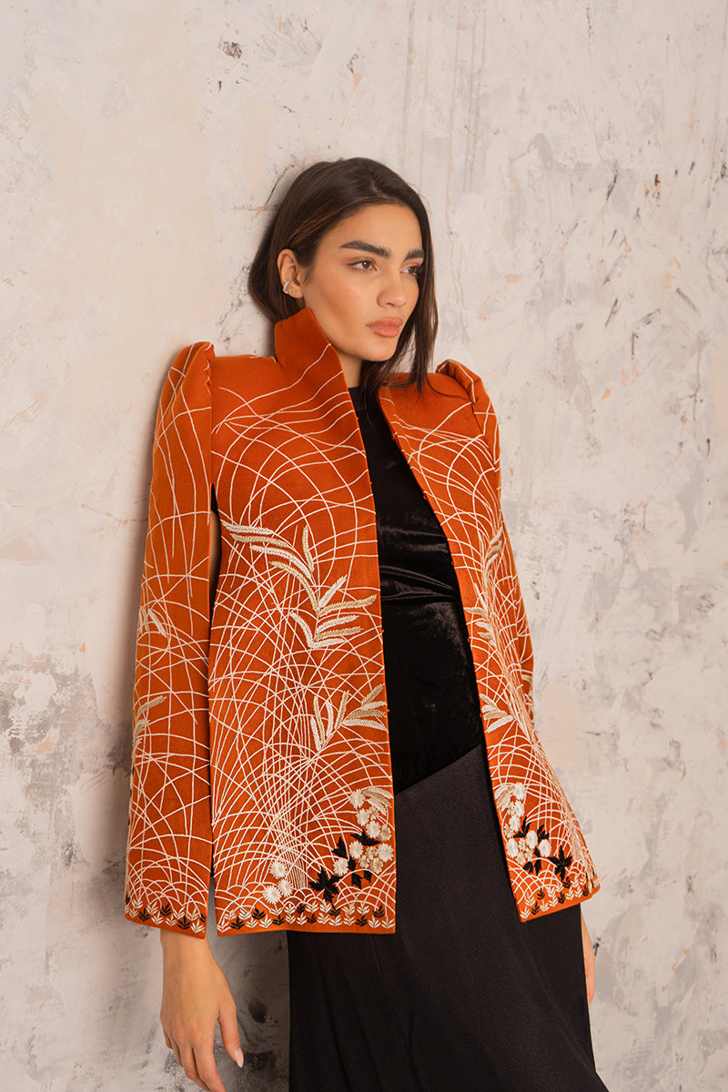 Nadya Shah Clementine Cape jacket in vibrant orange with wide collar and flowing design, displayed on a hanger.