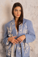 Nadya Shah Nyla powder blue belted jacket displayed hanging, featuring a tailored fit and stylish belt detail.