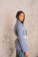 Nadya Shah Nyla powder blue belted jacket displayed on a hanger with front view and belt detail.