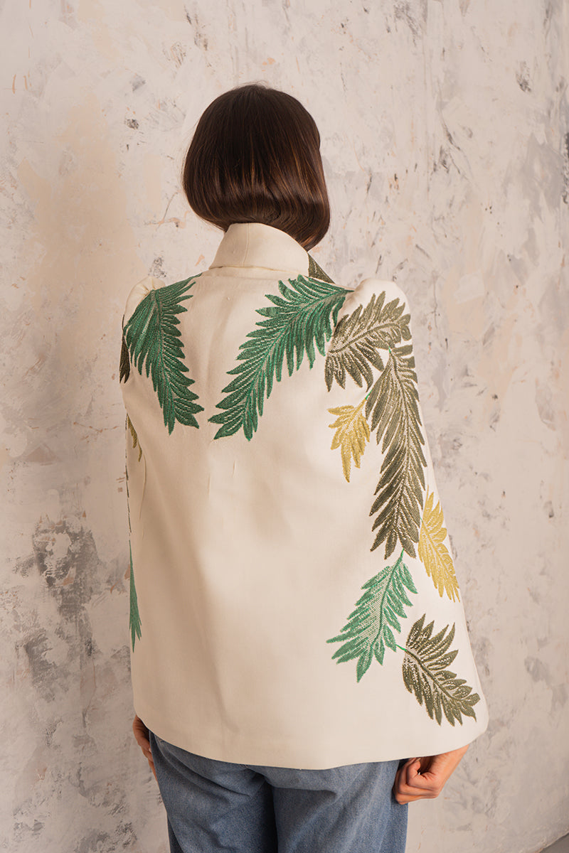 Nadya Shah Cara Leaf Cape jacket displayed on a hanger, featuring a leaf pattern and lightweight fabric for stylish layering.