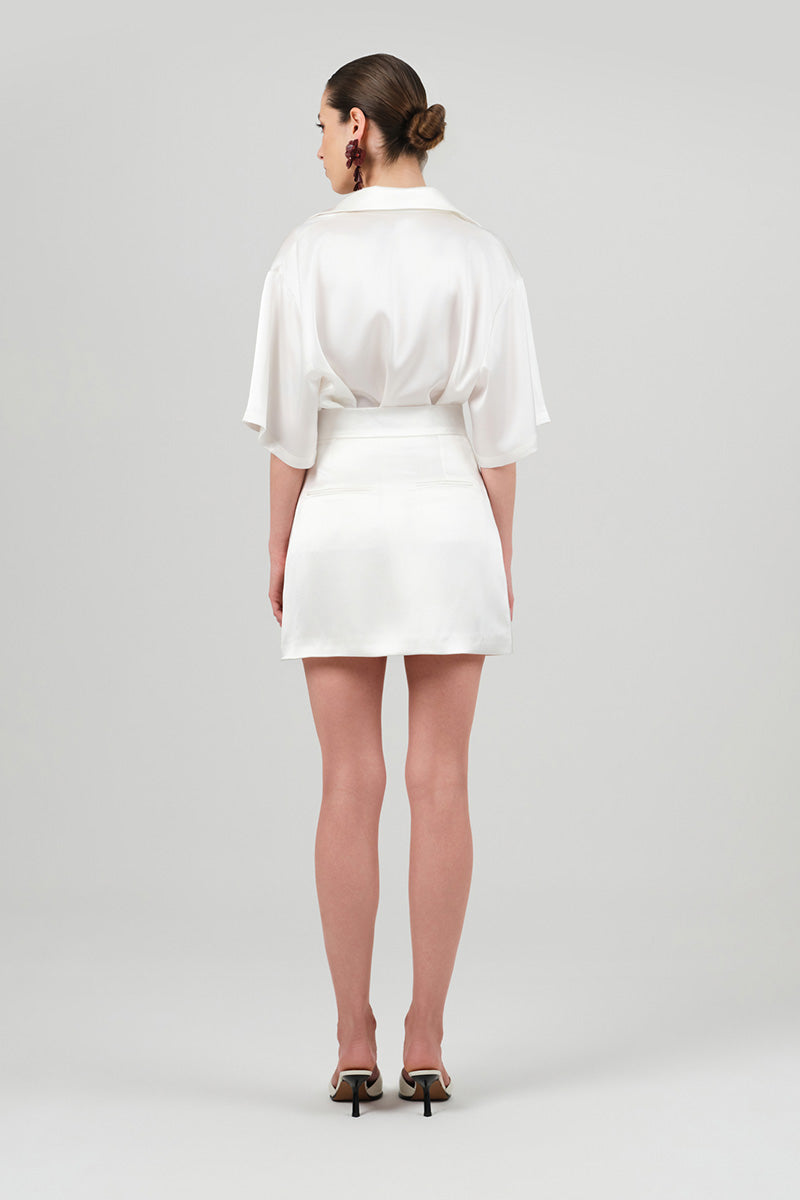White satin mini skirt from Izakova's Atena collection, shown on a model with a smooth, shiny fabric and stylish fit.
