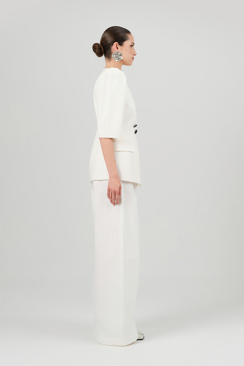 White Tessa pants by Izakova with a relaxed fit, shown on a model, featuring a smooth fabric and classic waistband.