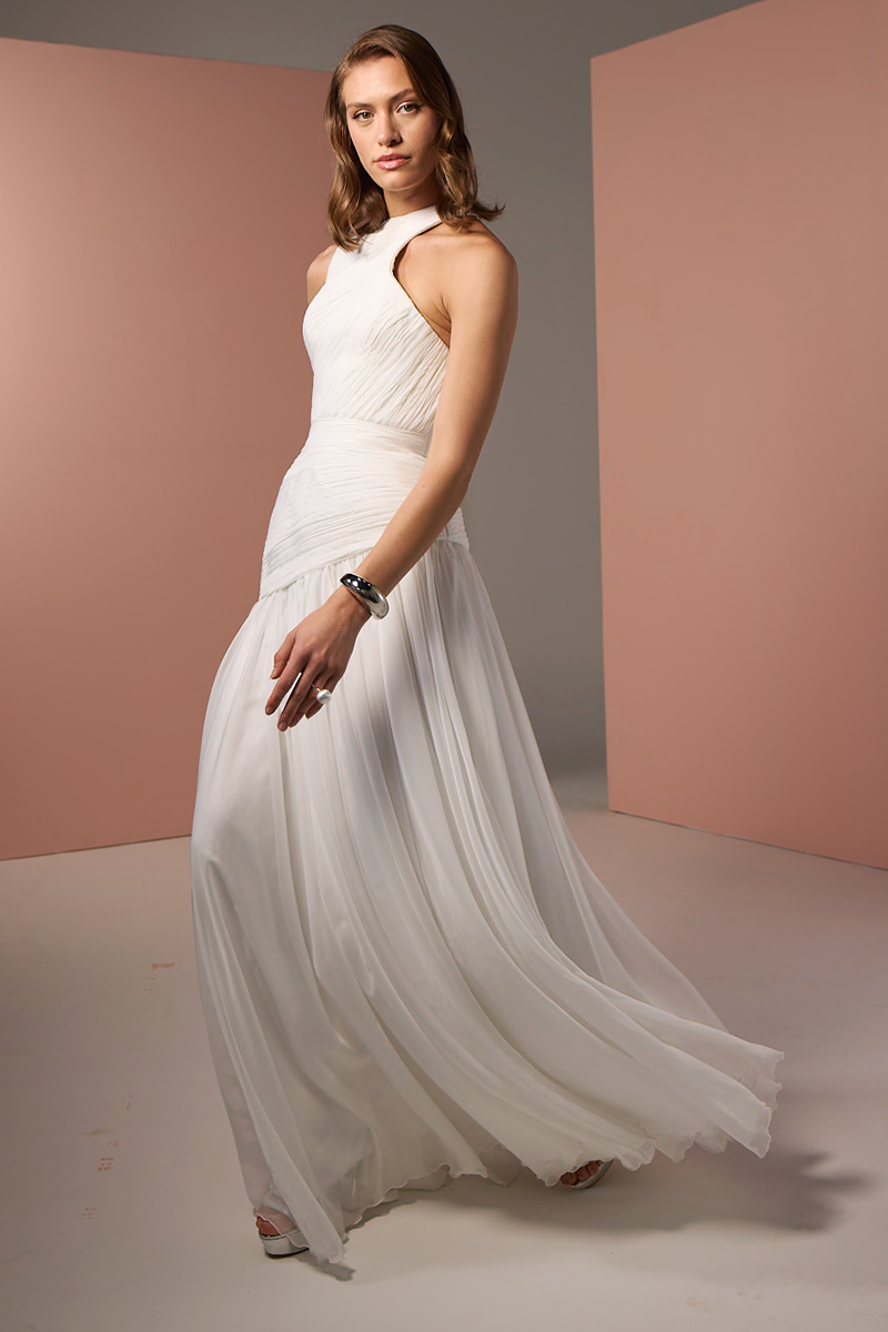 White asymmetrical low waistline gown by Joanna Andraos featuring a flowing design and elegant drape.