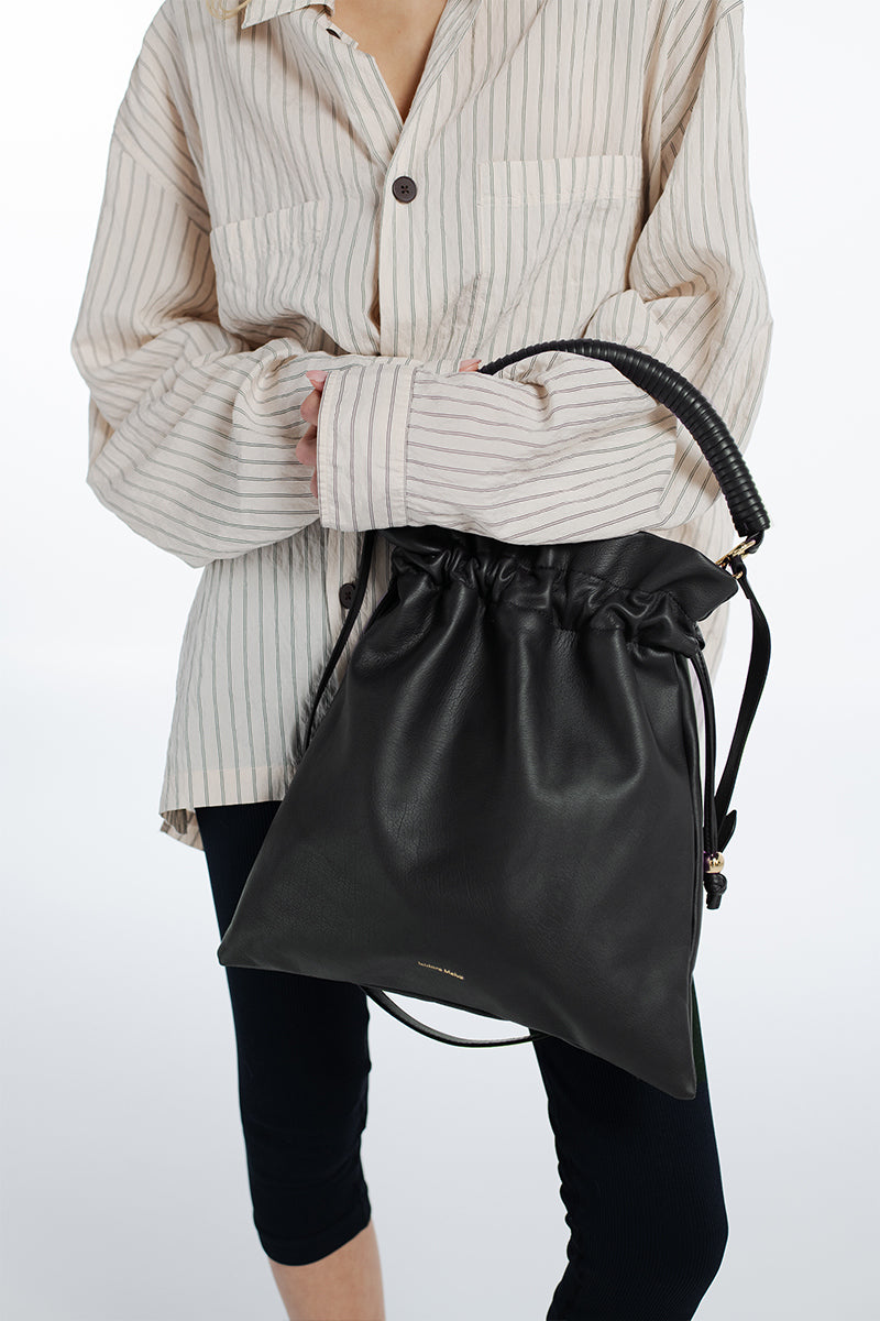 Black Elena pouch top handle bag by Isidora Malva, featuring a sleek design with top handle and compact size.