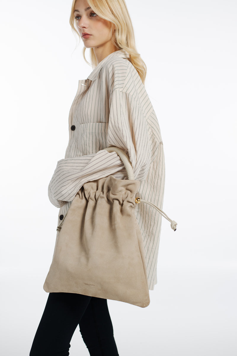 ISIDORA MALVA Elena suede pouch in nude with a top handle, showcasing soft suede material and elegant design.