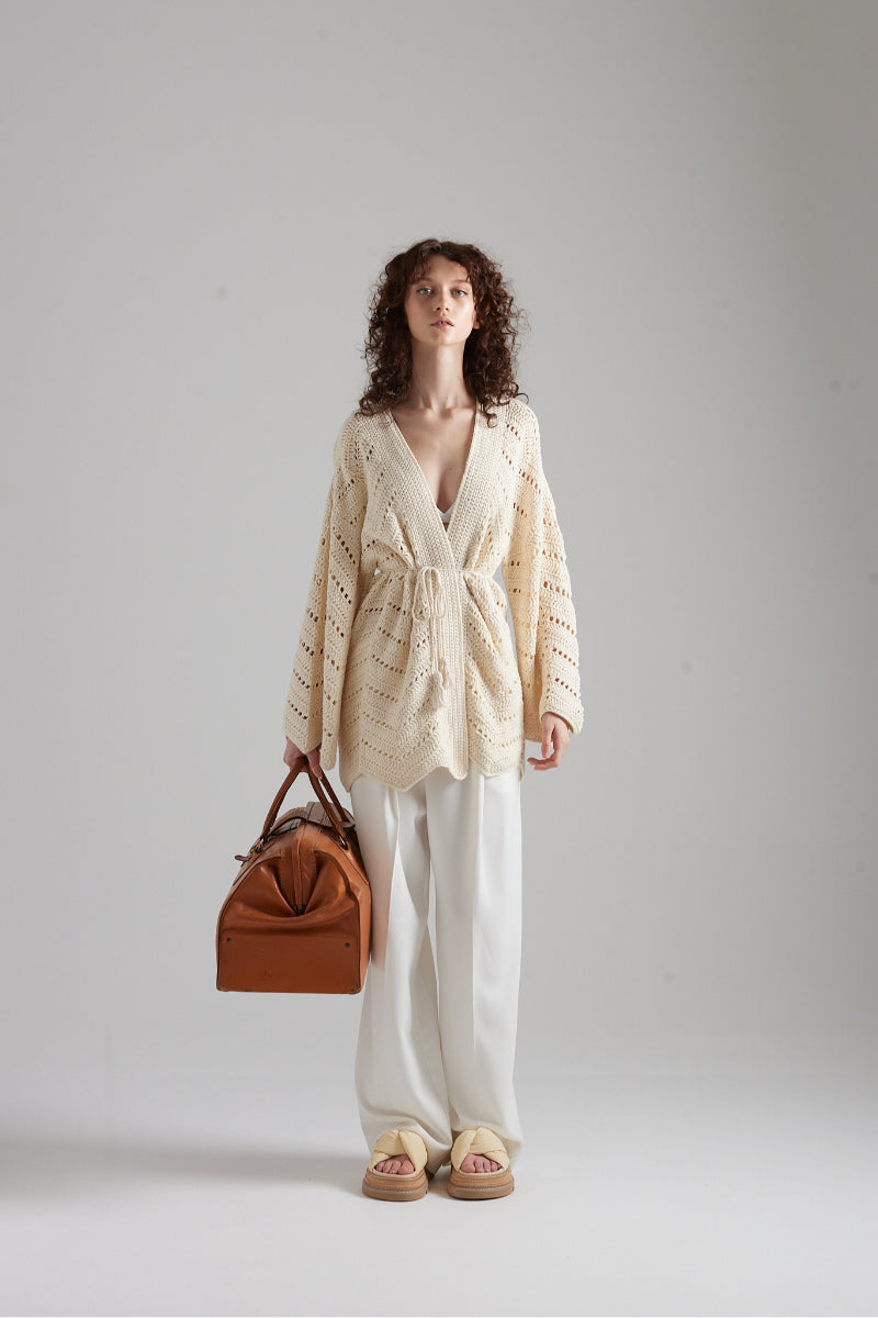 Soft beige MIA cardigan by First Born Knits, featuring a cozy knit texture and relaxed fit, displayed on a wooden background.