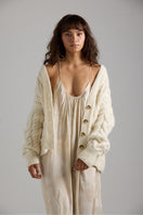 Light beige Paris cardigan by First Born Knits with a cozy, button-up design and ribbed cuffs, displayed on a neutral background.