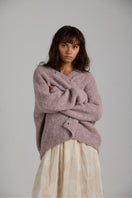 Purple Coco cardigan by First Born Knits, soft knitwear with a cozy fit, shown on a hanger with a textured background.
