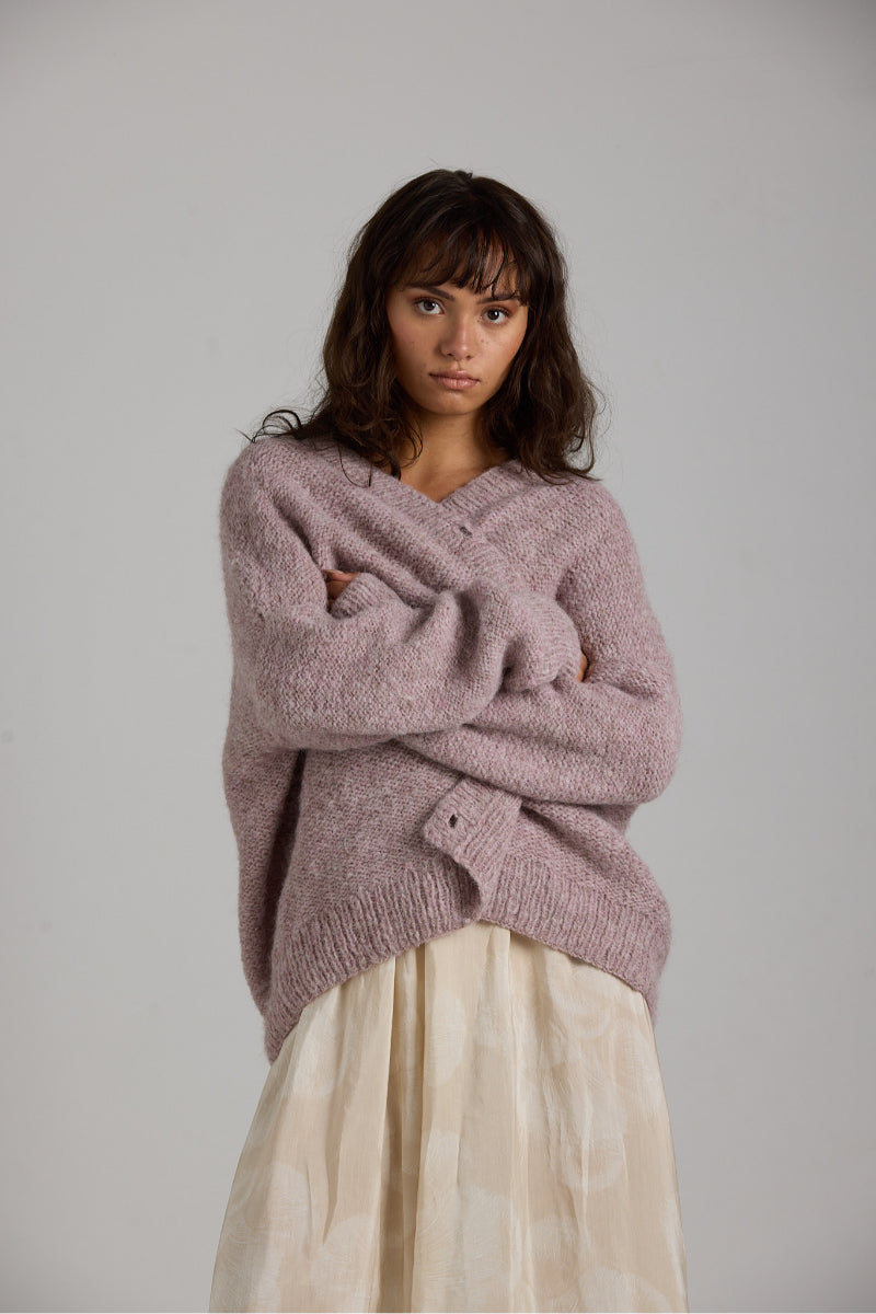 Purple Coco cardigan by First Born Knits, soft knitwear with a cozy fit, shown on a hanger with a textured background.