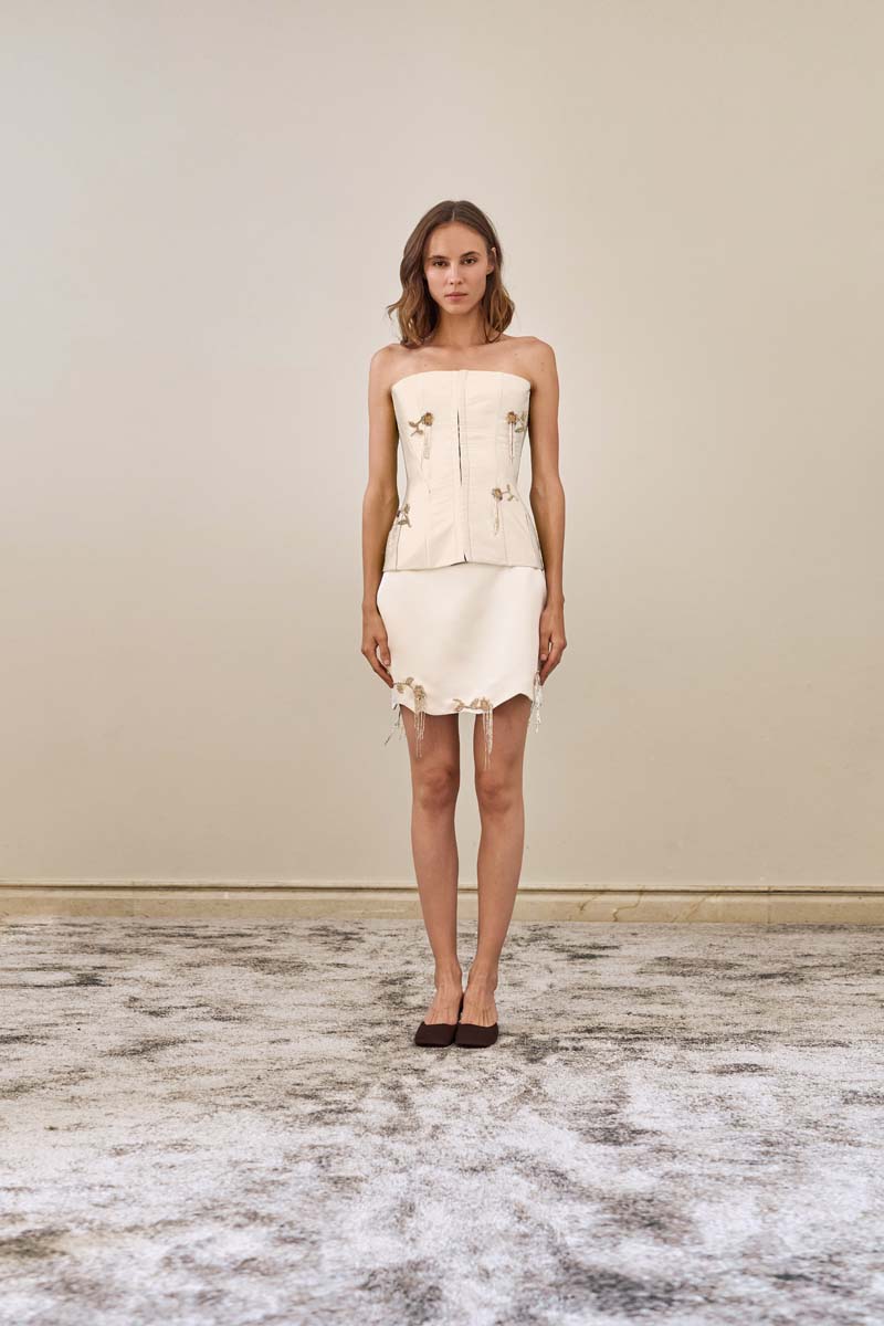 White fold mini skirt by YASSMIN SALEH, shown from the front, highlighting its stylish fold design and clean ivory color.