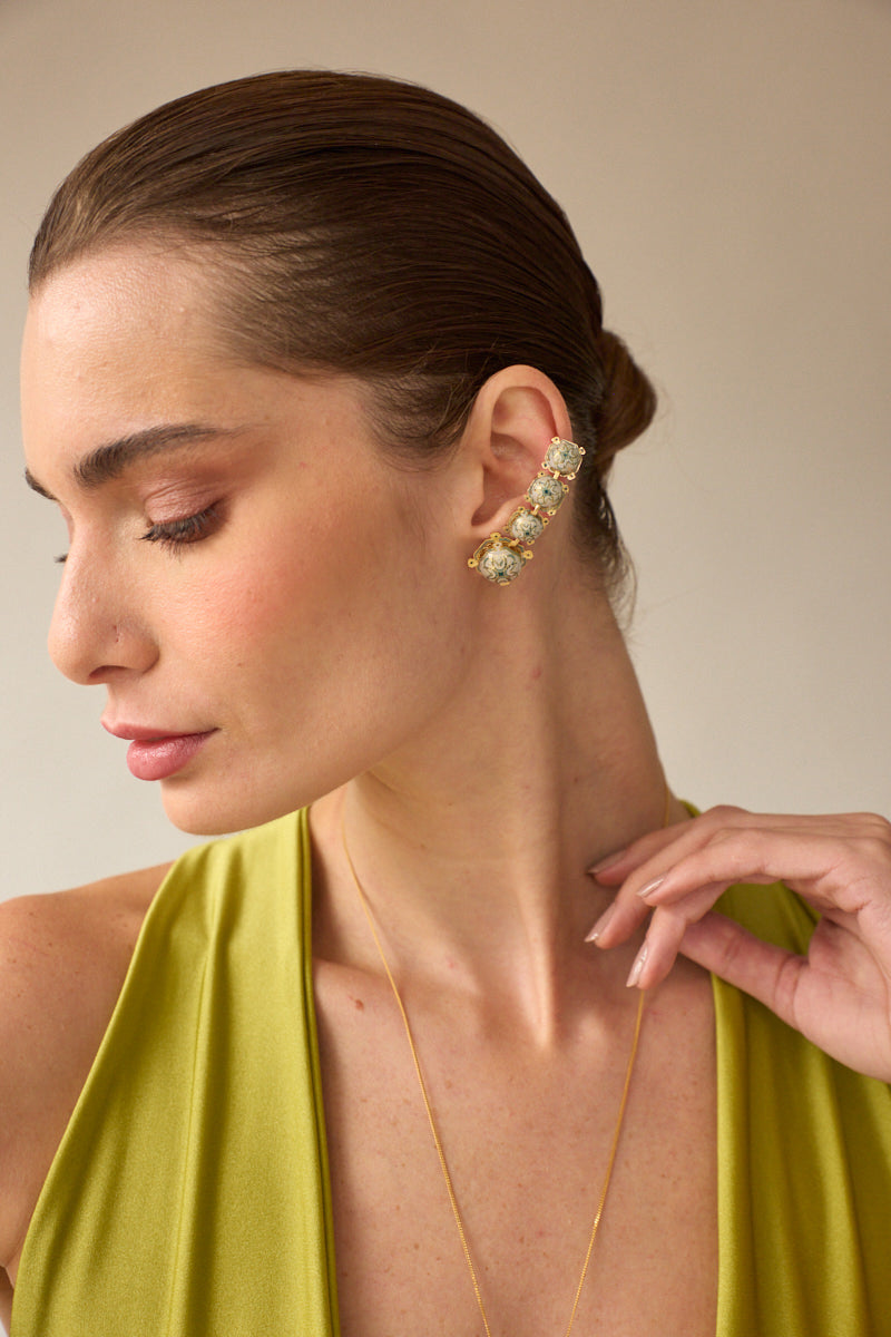 Green talisman ear cuff by Álvaro Ávila, featuring intricate design and worn on the ear for a stylish accessory look.