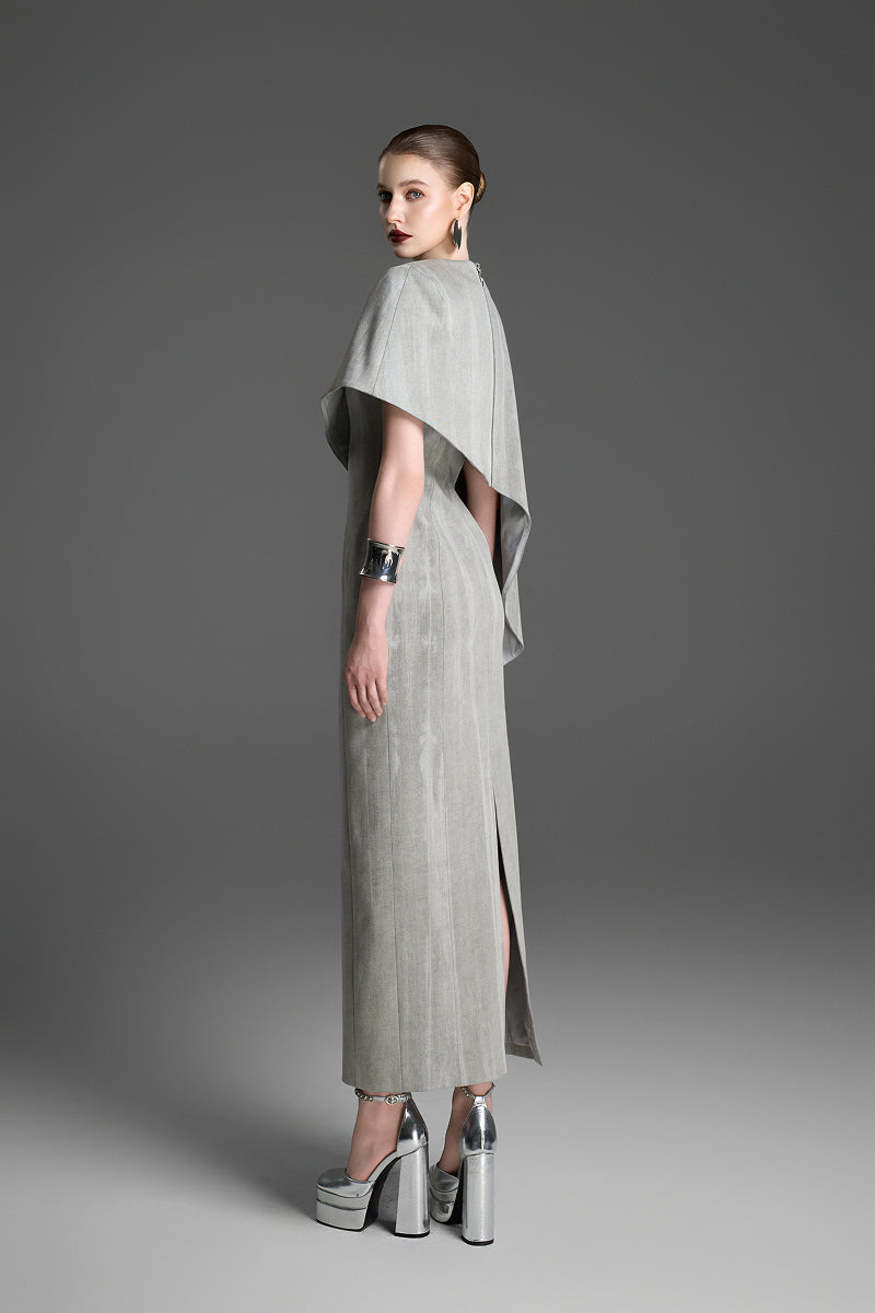 Light gray asymmetrical draped cape sleeve maxi dress by GVLUX, featuring a sleek column silhouette and elegant design.