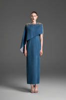 Blue asymmetrical maxi dress with draped cape sleeve by GVLUX, featuring a flowing silhouette and elegant design.