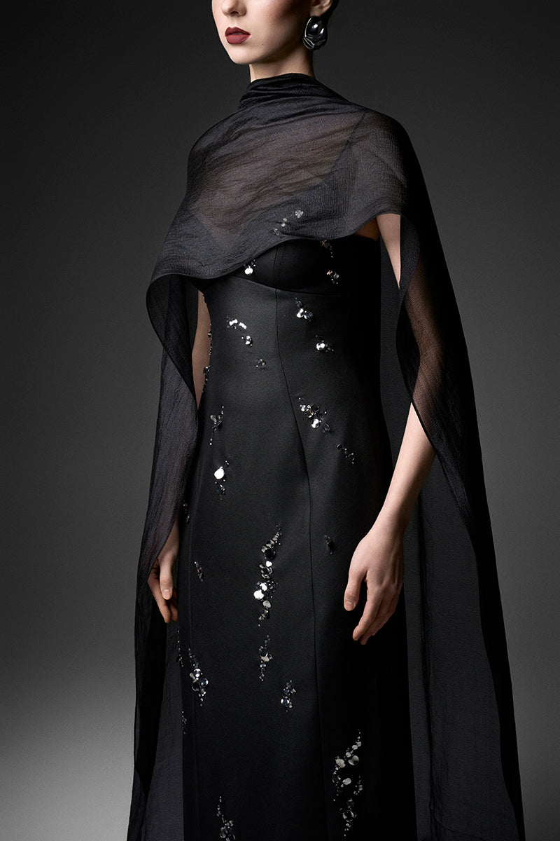 Black cape neck column gown by GVLUX, featuring elegant long silhouette and sleek design, perfect for formal occasions.
