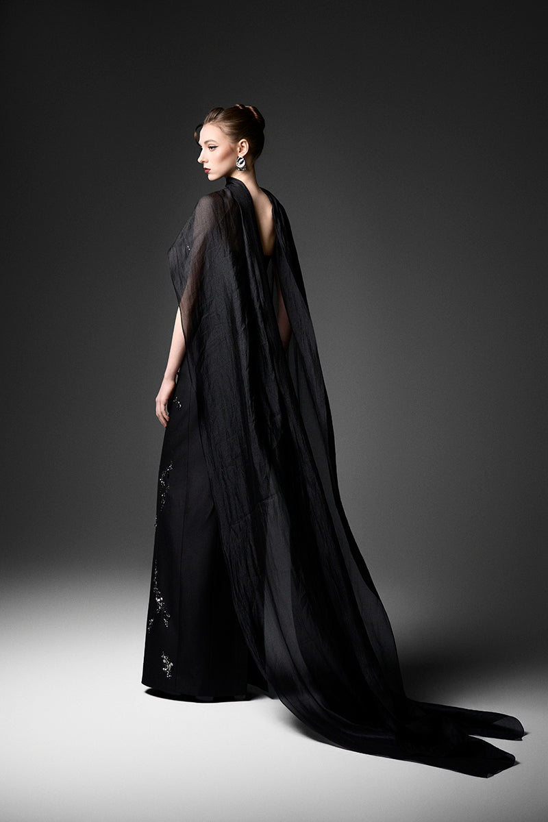 Black Cape Neck Column Gown by GVLUX, elegant evening dress with sleek silhouette and flowing fabric, perfect for formal events.
