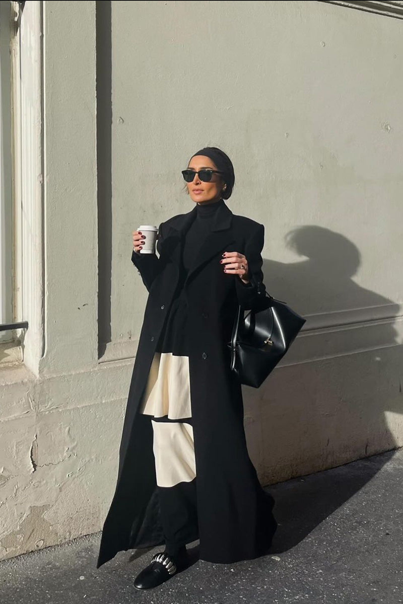 Black straight-cut coat by Kris Marán featuring signature buttons, shown on a model with a classic, tailored design.