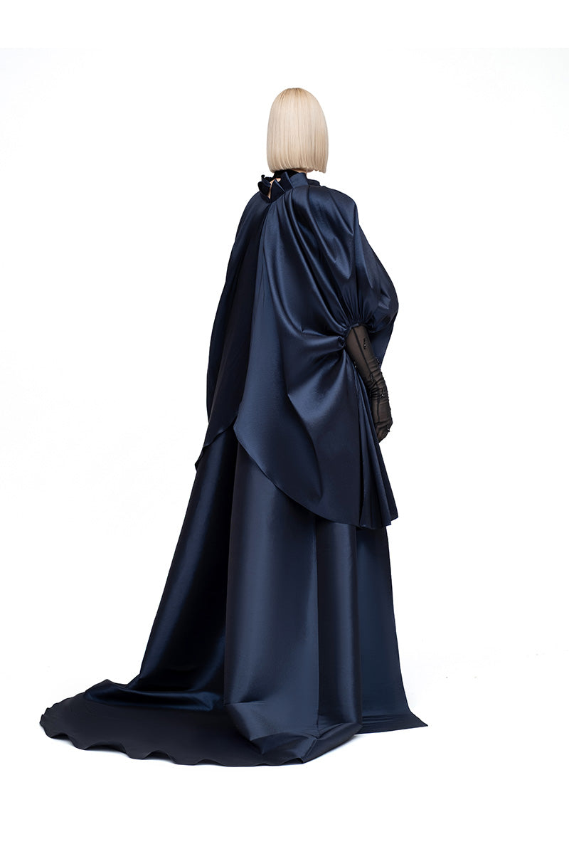 Navy Lotus Cape jacket by MOON / HAKAN YILDIRIM, featuring a flowing fabric and stylish design, draped on a hanger.