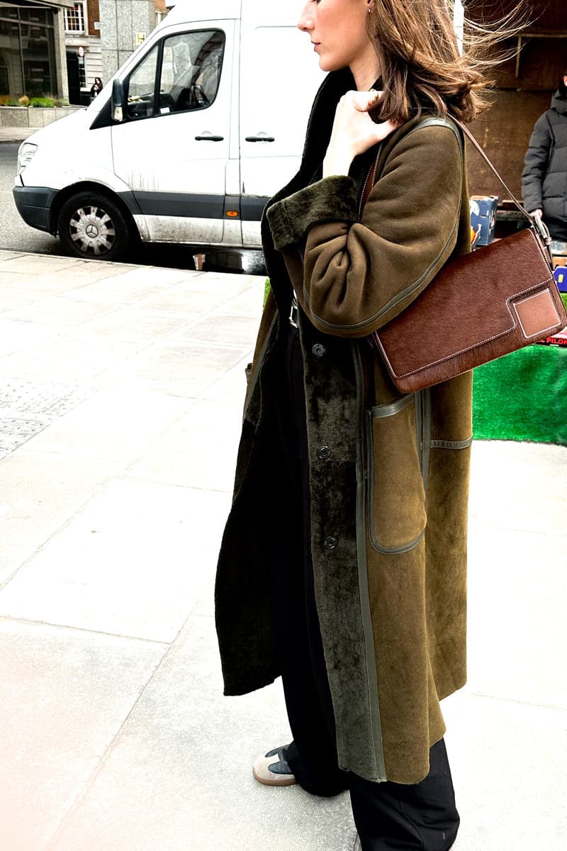 Verheyen Zina Biker Green Shearling Coat displayed on a hanger with a plush green shearling collar and stylish leather exterior.