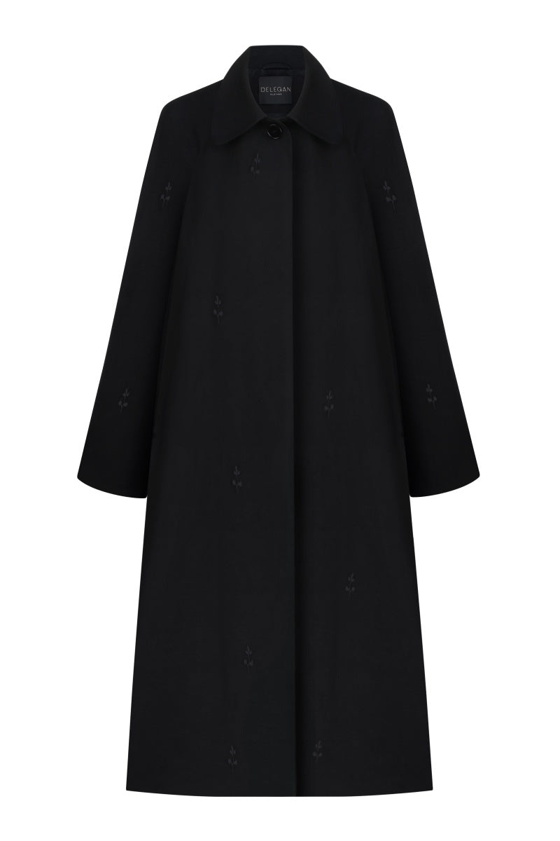 Black trench coat by Delegan hanging on a wooden hanger, showcasing classic design and tailored fit.