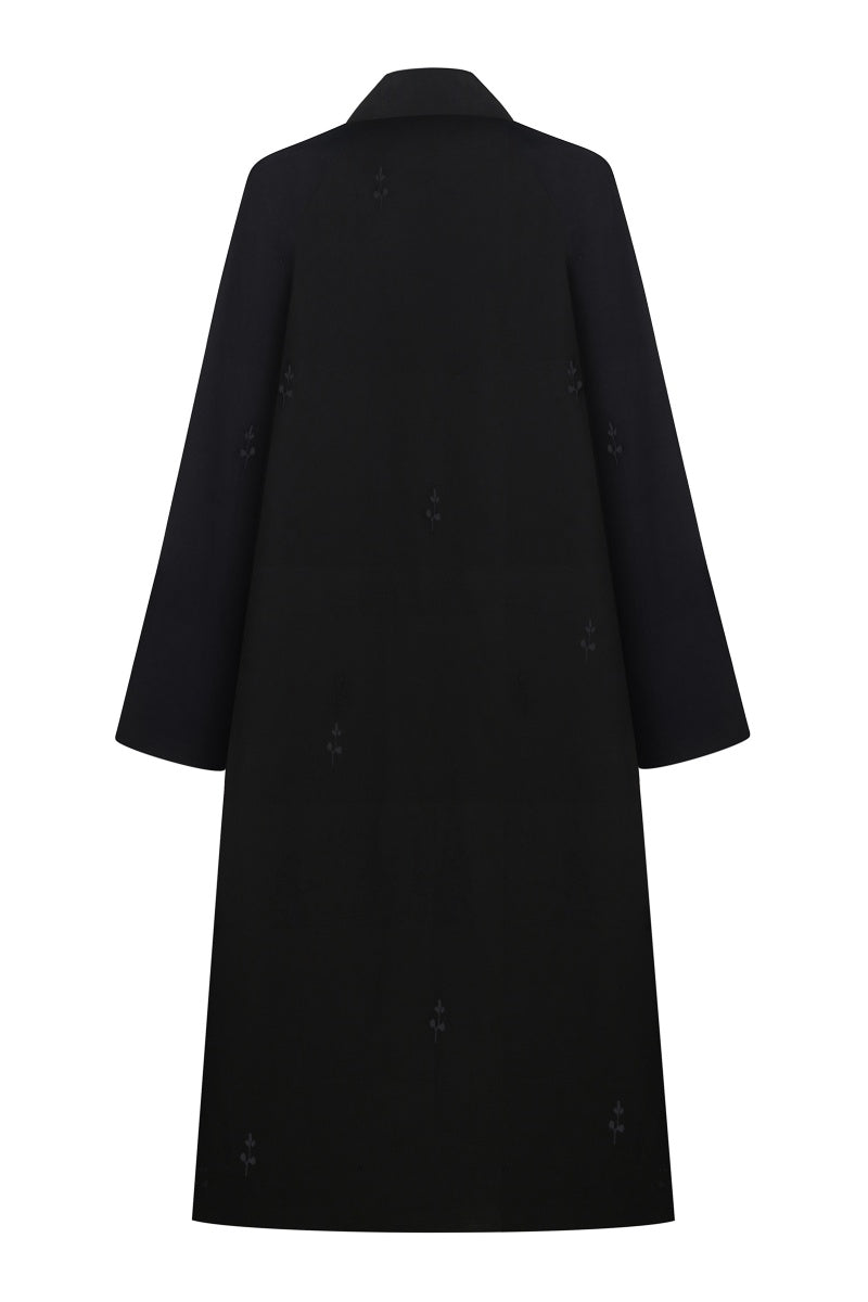 Black trench coat by Delegan, shown on a hanger with a classic double-breasted design and belt details, full-length view.