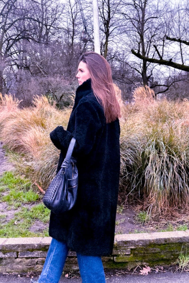 Black Verheyen Zina biker shearling coat with wide lapels and zip details, shown on a model standing outdoors.