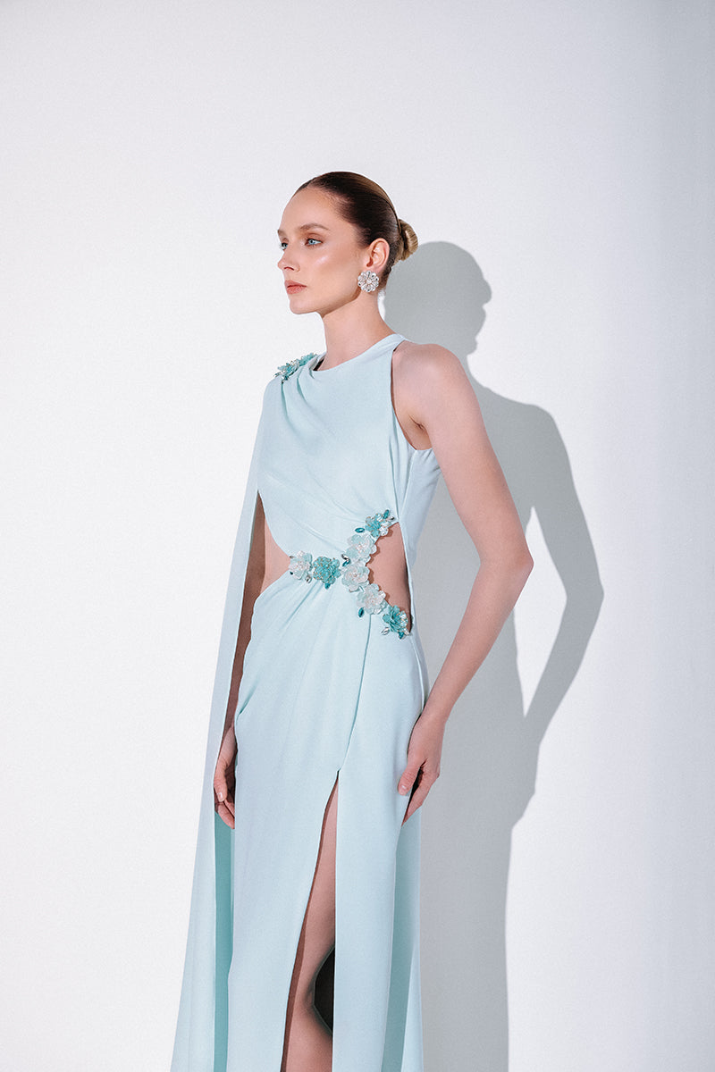Blue embellished cape gown by Monika Dimova, featuring intricate beadwork and flowing fabric, elegant evening wear for special occasions.