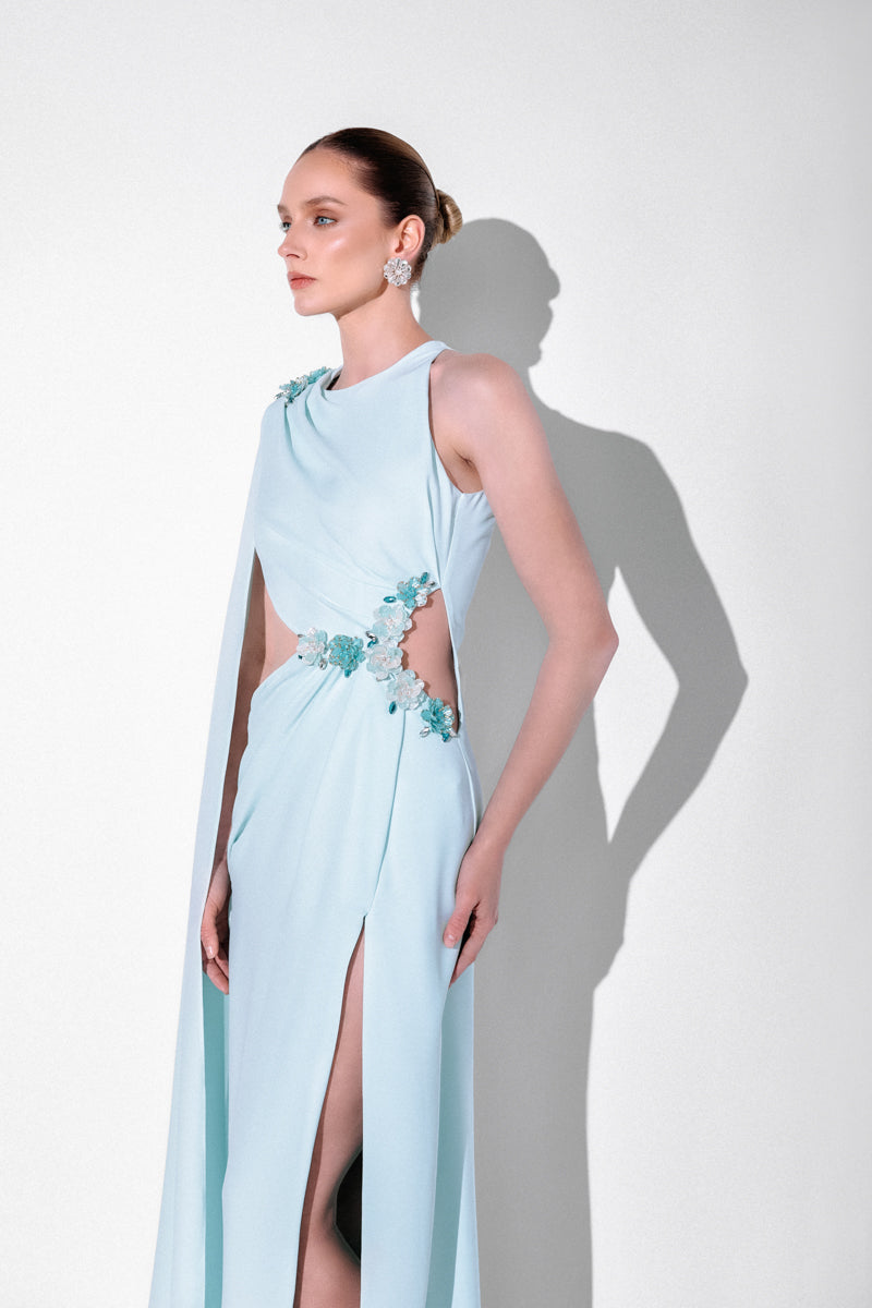 Blue embellished cape gown by Monika Dimova, featuring intricate beadwork and flowing fabric, perfect for elegant occasions.