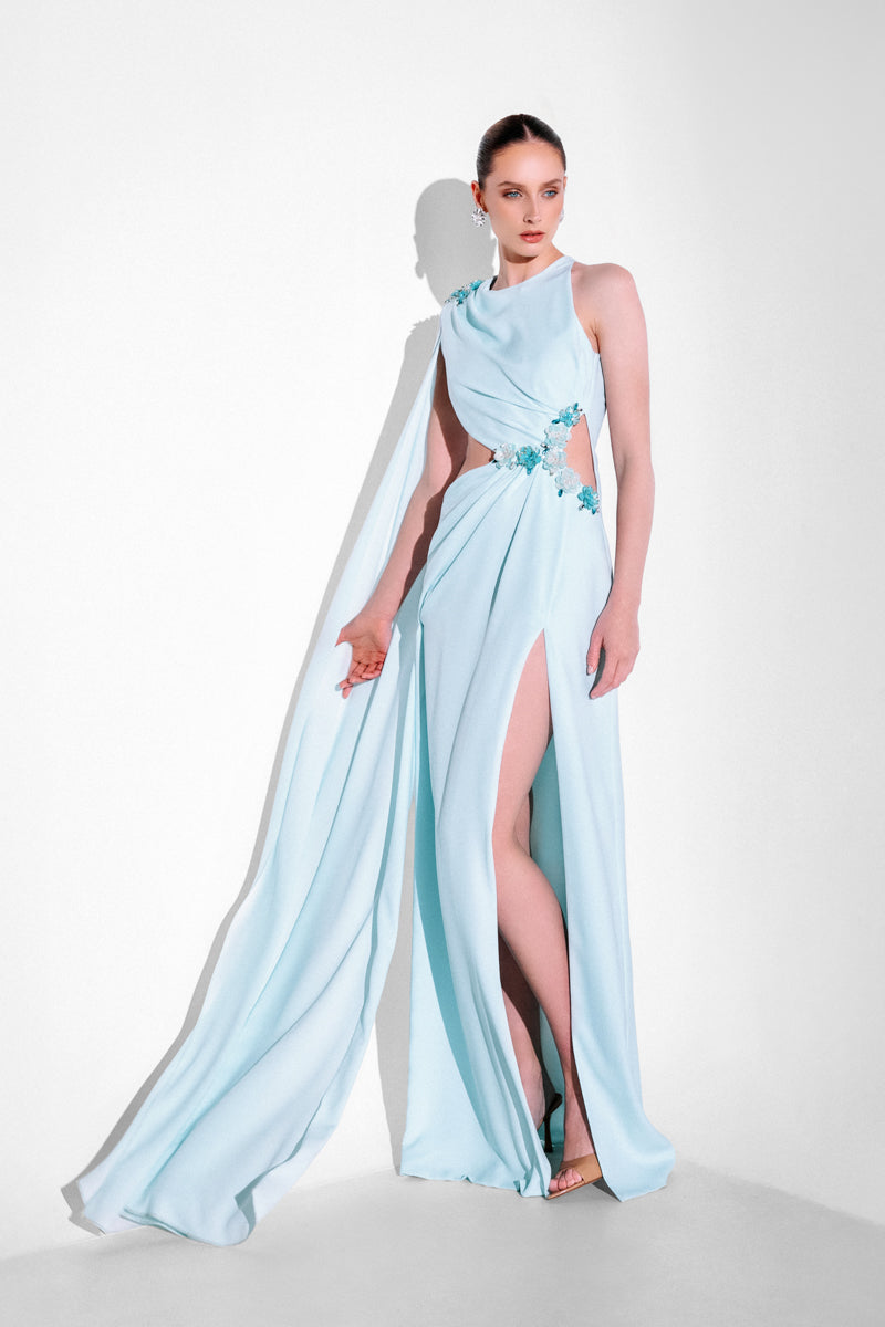 Blue embellished cape gown by Monika Dimova featuring intricate beadwork and flowing fabric, elegant formal evening attire.