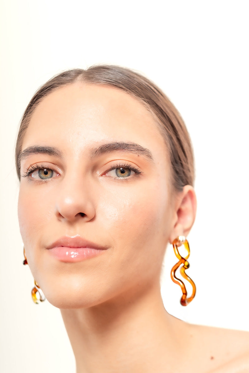 Salvária Interconexión L amber earrings featuring intricate design and warm amber stones on silver hooks.