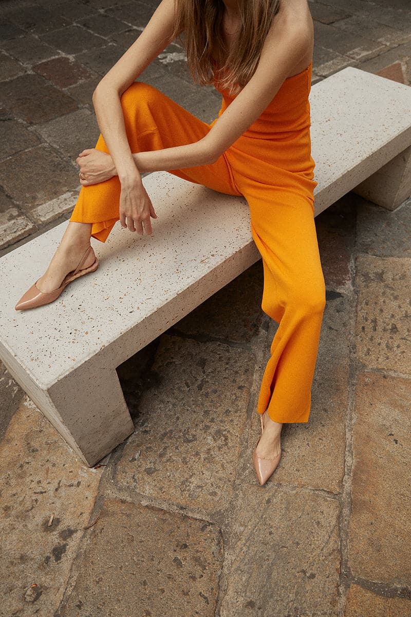 A pair of AERA Jackie Nude patent-effect slingback flats with pointed toes and ankle straps, showcasing sleek, shiny footwear.