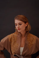 Ecru belted jacket by Nadya Shah featuring a structured design and front pockets, shown on a model in a casual outdoor setting.